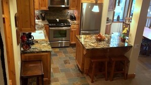 A kitchen with granite countertops, wooden cabinets, a stainless steel refrigerator, and a built-in oven. - 114 Premium Condo (Mammoth Lakes)