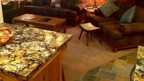 A cozy attic-style living room with wooden walls, a fireplace, a sofa, and a dining area with a granite countertop. - 114 Premium Condo (Mammoth Lakes)