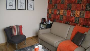 Una sala de estar con sofá, sillón, mesa de centro y una pared decorada con cuadros.