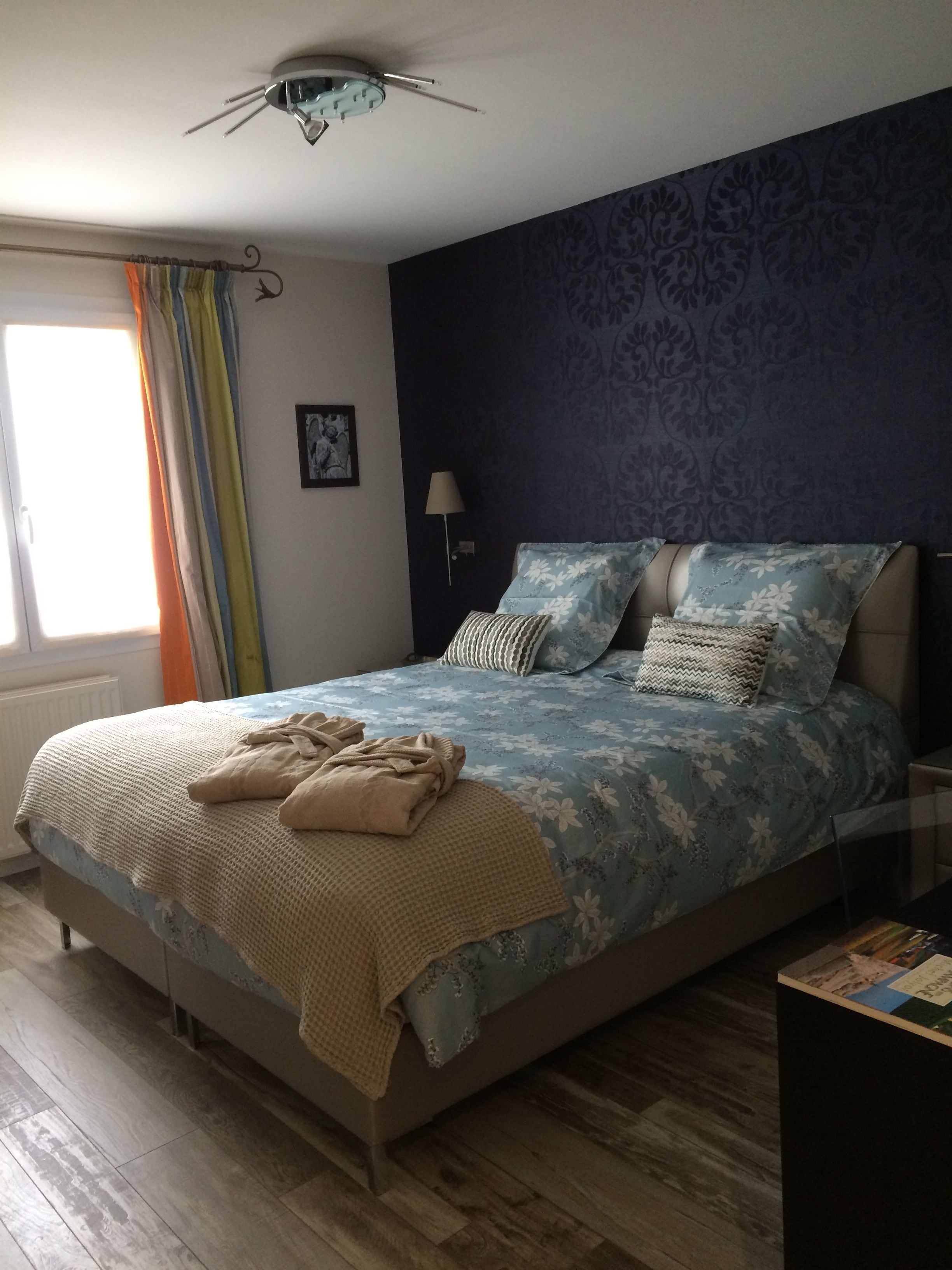 Ein Schlafzimmer mit Bett, Nachttisch, Lampe, einem Fenster mit Vorhängen und einem Deckenventilator.