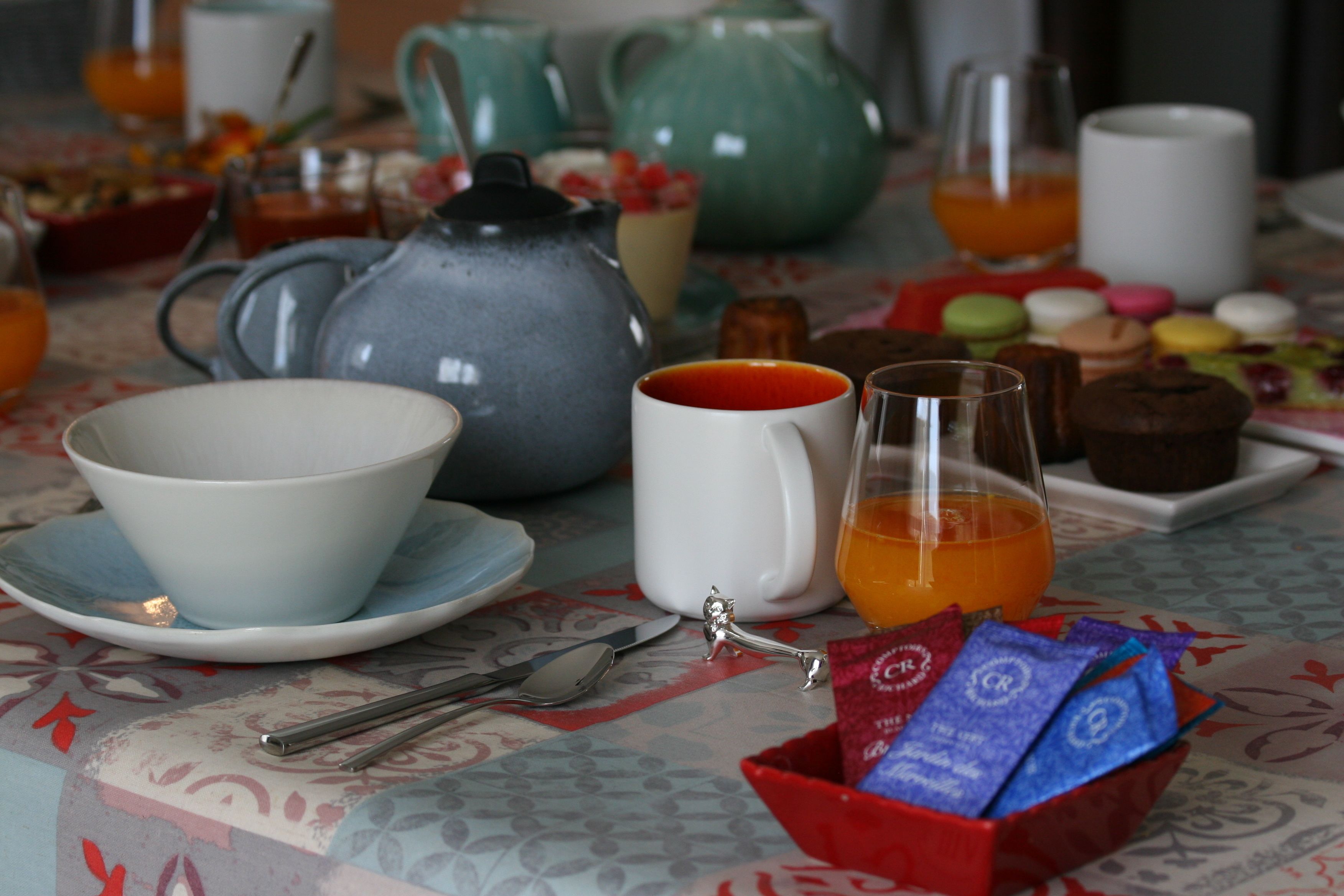 Una mesa dispuesta con tetera, tazas, vaso de jugo de naranja, un muffin y un cuenco de bocadillos.