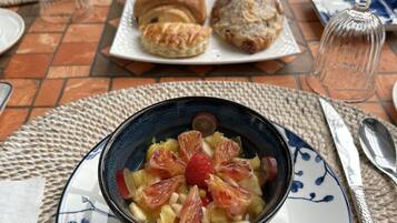 A table set with pastries, a bowl of fruit salad, and a teapot.