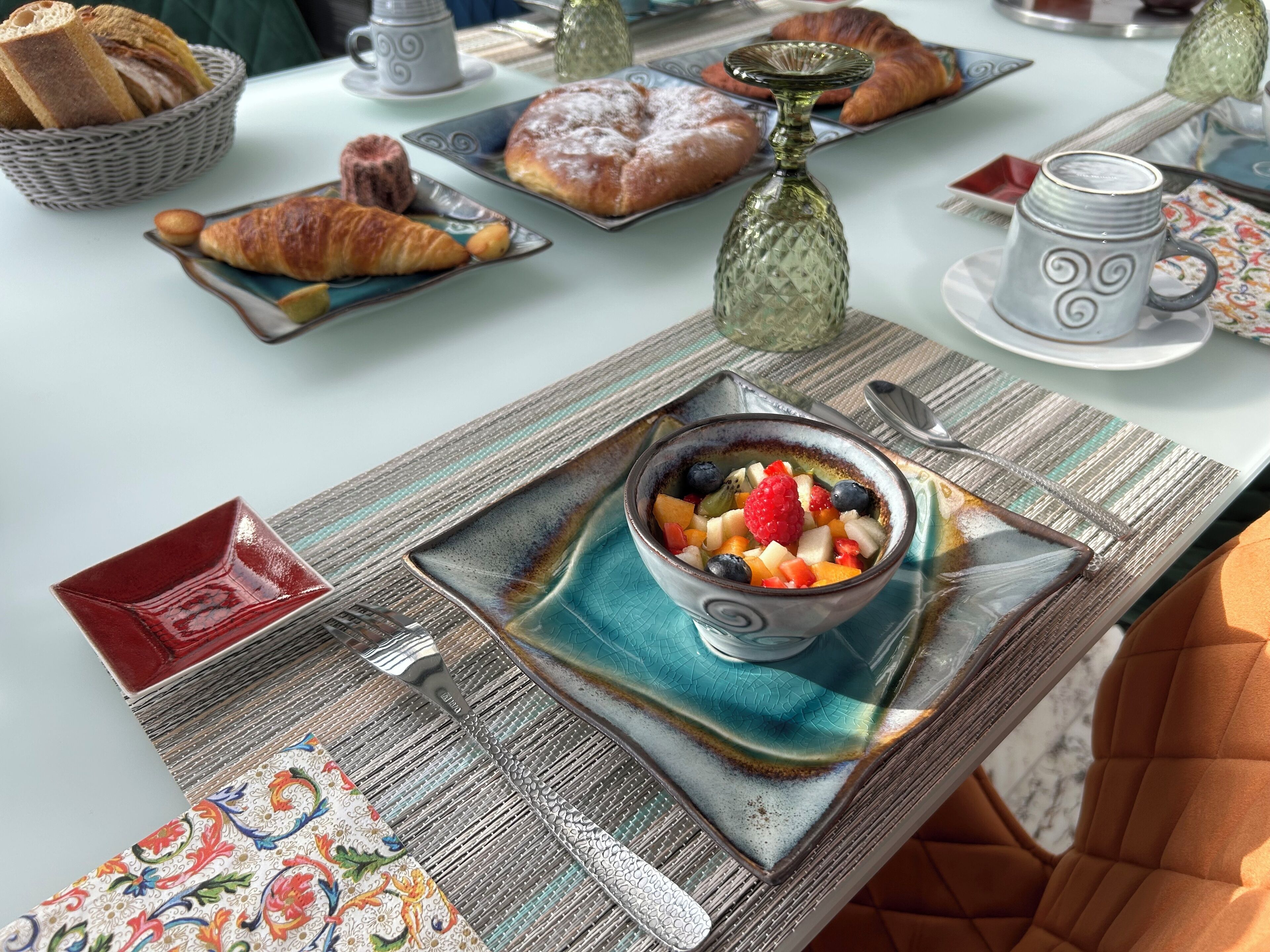 Une table de petit-déjeuner avec des croissants, des viennoiseries, un panier de fruits et une tasse de café.