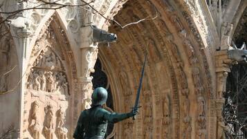 Une statue d’un chevalier à cheval, placée devant un bâtiment de style gothique orné de sculptures complexes en pierre.
