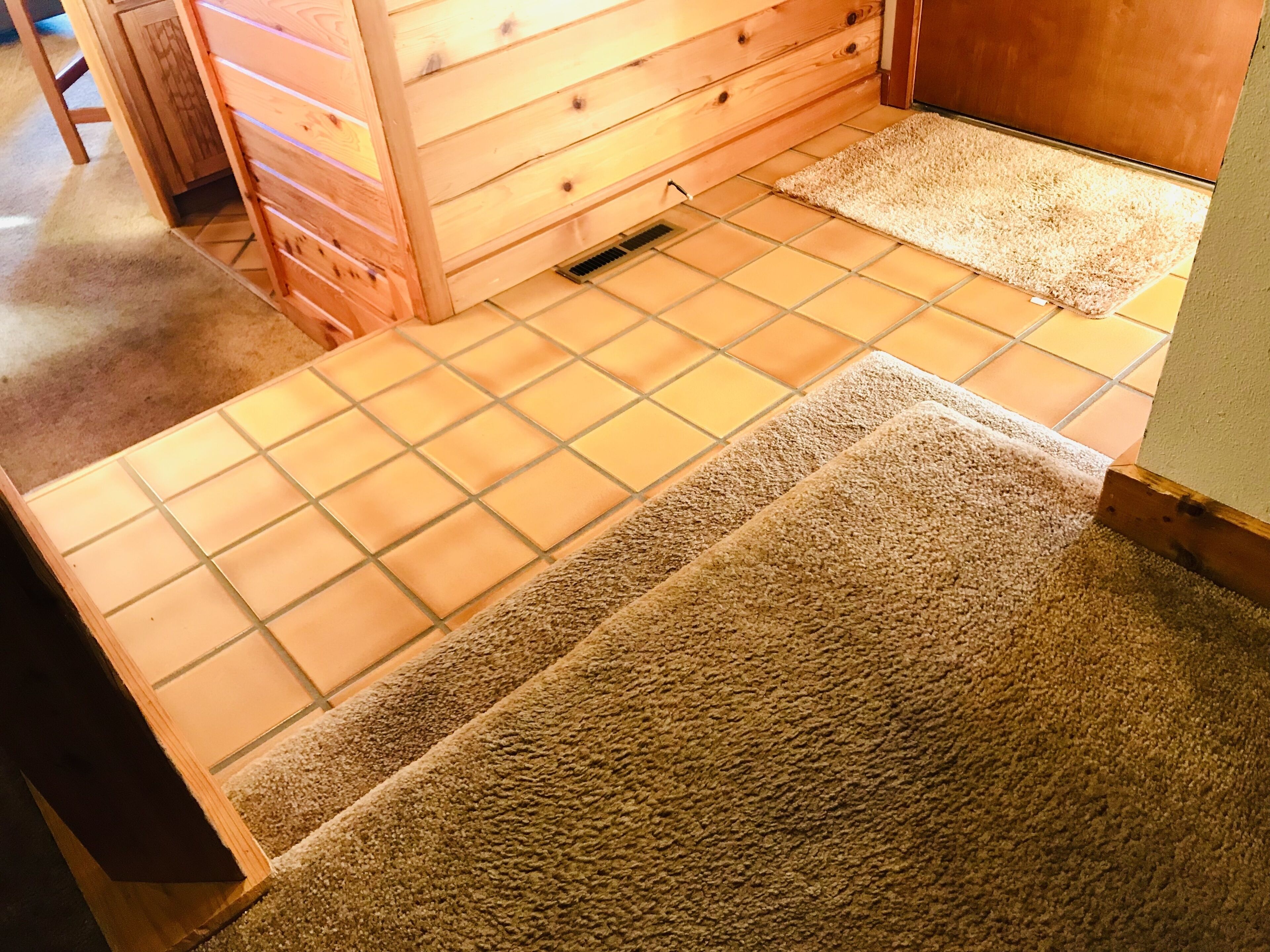 A room with a tiled floor, a wooden dresser, and a carpeted area.