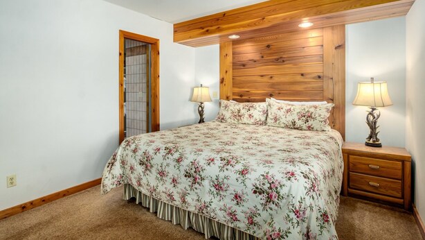 A bedroom with a wooden headboard, floral bedding, two bedside lamps, and a carpeted floor. - Stutzhaven in the Mountains - 2 Br Home (Estes Park)