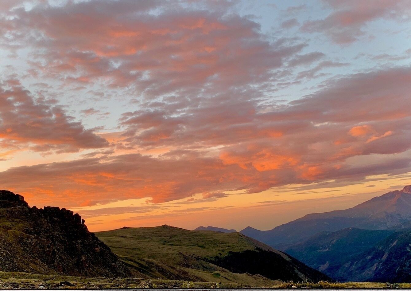 A mountainous landscape with rolling hills and a sunset sky.