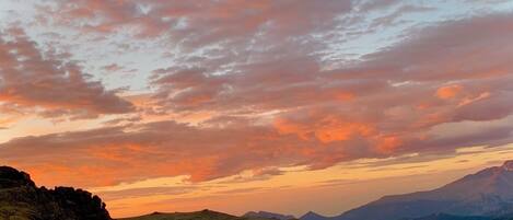 A mountainous landscape with rolling hills and a sunset sky.