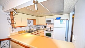 A compact kitchen with a central island, a microwave, a stove, and a refrigerator. - Thunder Island 10A (Ocean City)