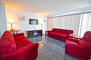Ein modernes Wohnzimmer mit einer roten Sofagarnitur, einem Flachbildfernseher und einem großen Fenster mit Jalousien.