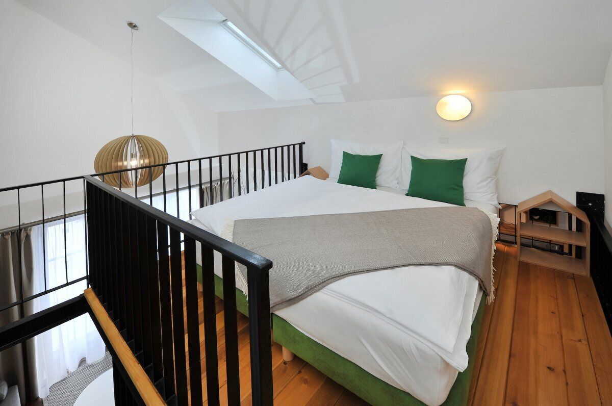 Un dormitorio con tragaluz, cama con ropa de cama verde y blanca, lámpara colgante y una pequeña estructura de madera.