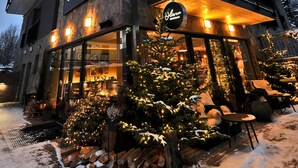 Un edificio de varios pisos con letrero de restaurante, mesas al aire libre y suelo cubierto de nieve.