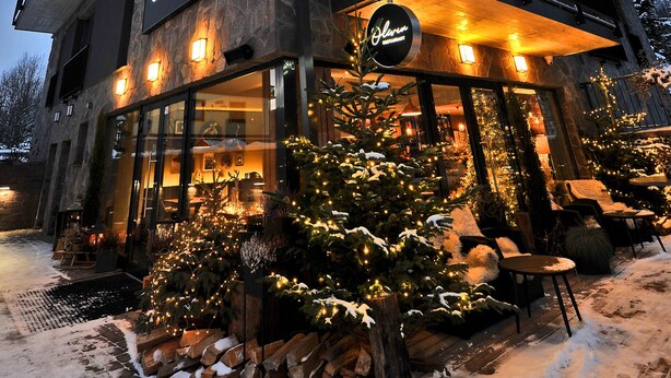 A multi-story building with a restaurant sign, outdoor seating, and snow-covered ground. - APLEND Vila Olivia (Vysoké Tatry)