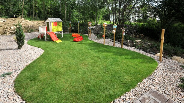 Un área verde bien cuidada con un parque infantil, que incluye un tobogán y una casita.