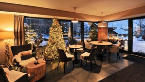 A modern living room with a large Christmas tree, comfortable seating, and a view of a snowy landscape through large windows. - APLEND Vila Olivia (Vysoké Tatry)