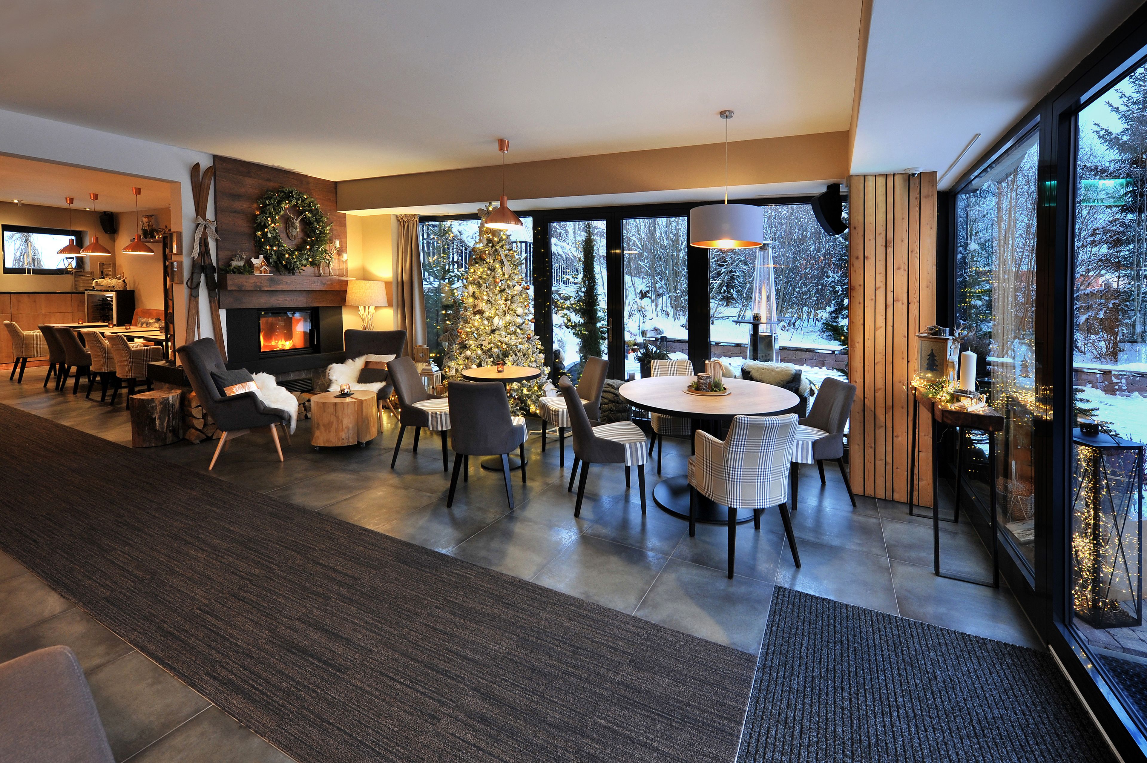 Een moderne woonkamer met een open haard, een kerstboom en grote ramen met uitzicht op het landschap.