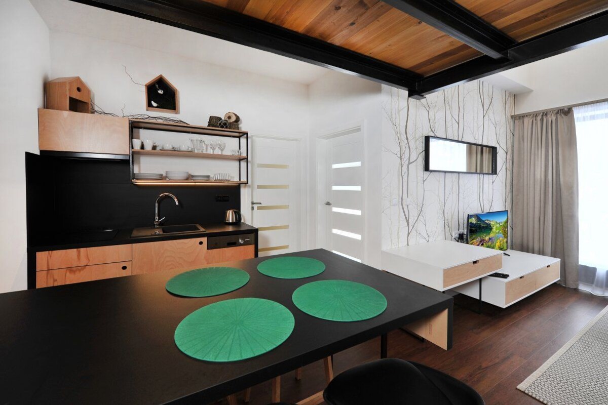 Una cocina moderna con encimera negra, armarios de madera y microondas integrado. Hay una mesa de comedor con individuales verdes y un televisor montado en la pared.