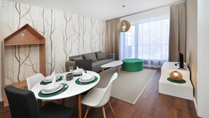 A modern living room with a dining area, a sofa, a TV, and a wooden bookshelf. - APLEND Vila Olivia (Vysoké Tatry)