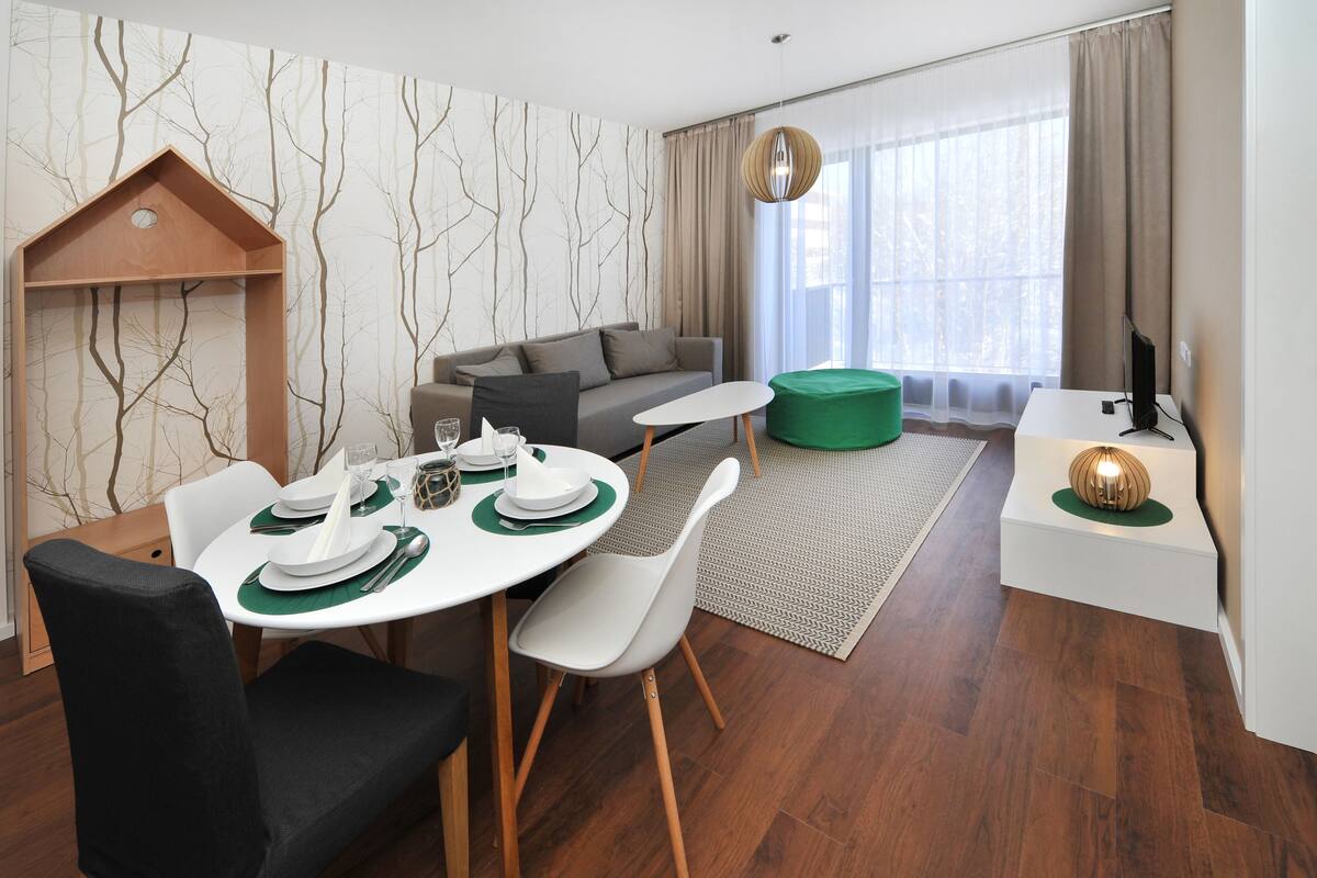 Una sala moderna con comedor, un sofá, un televisor y una estantería de madera.