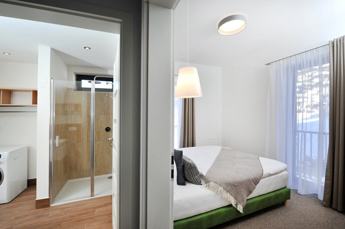 Un cuarto de hotel con una cama, ducha, lámpara y vistas por la ventana.