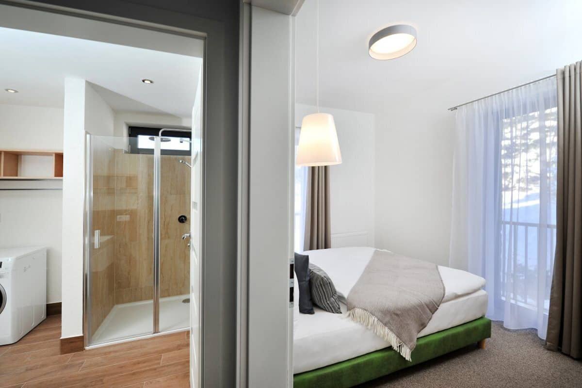 Un cuarto de hotel con una cama, ducha, lámpara y vistas por la ventana.