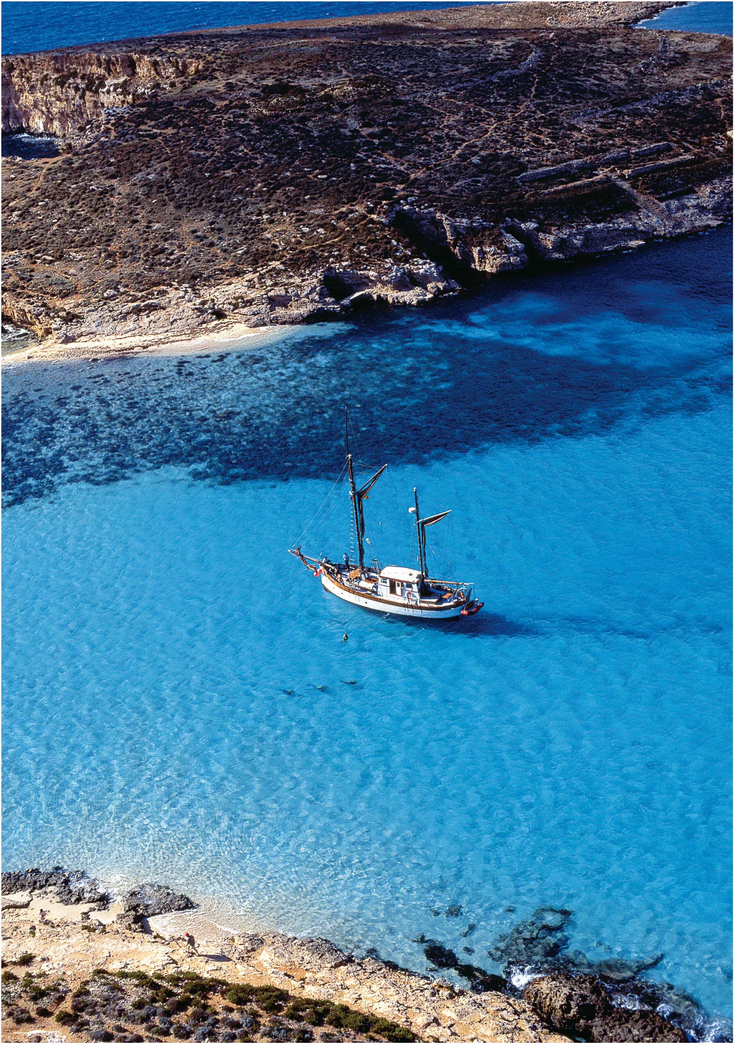A boat anchored in clear blue waters with rocky terrain in the background.