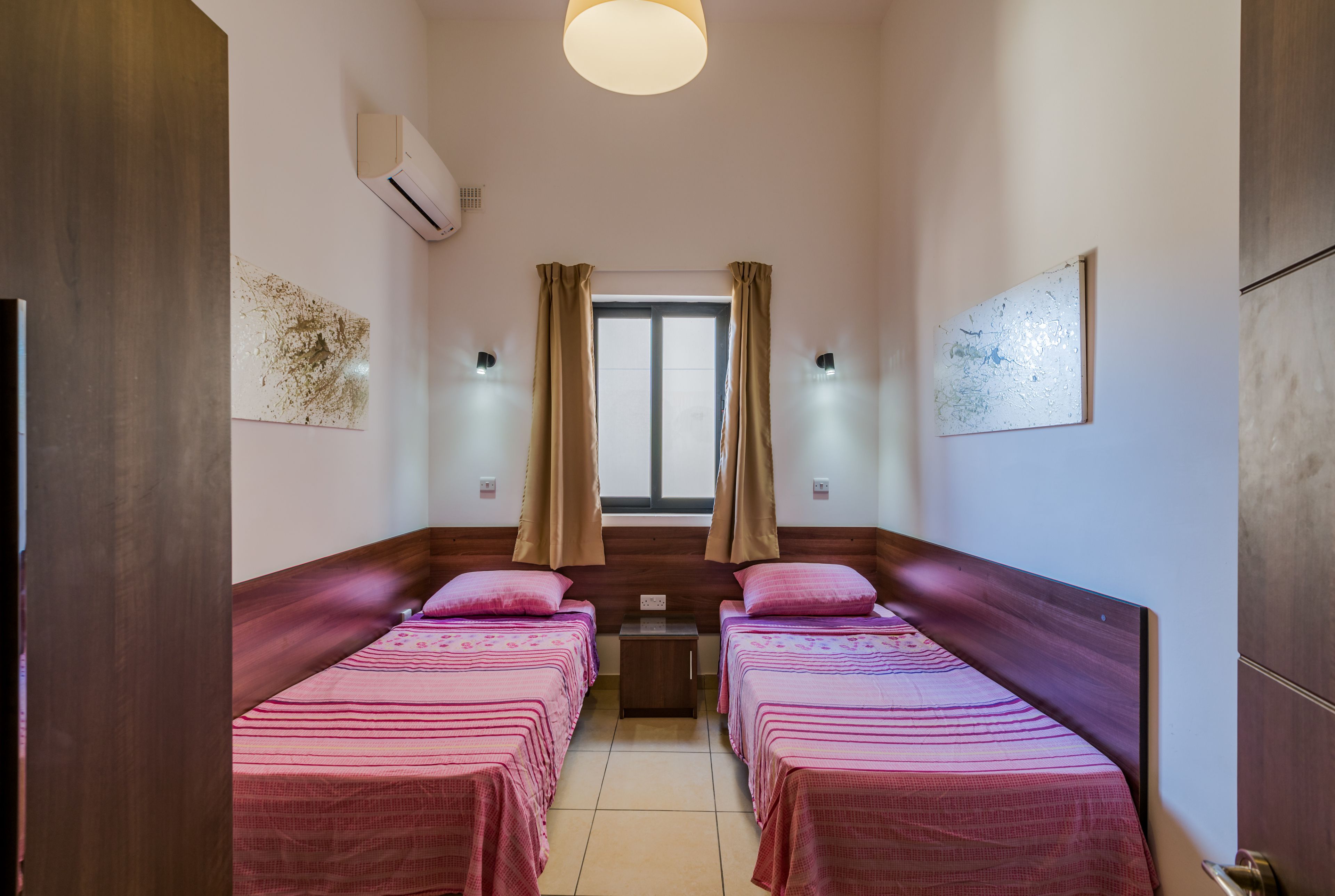 Una habitación con dos camas, una ventana con cortinas, aire acondicionado y una mesita.