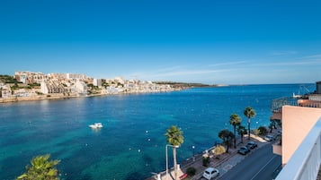 Un paisaje urbano costero con un mar azul cristalino, un barco y edificios a lo largo del malecón.