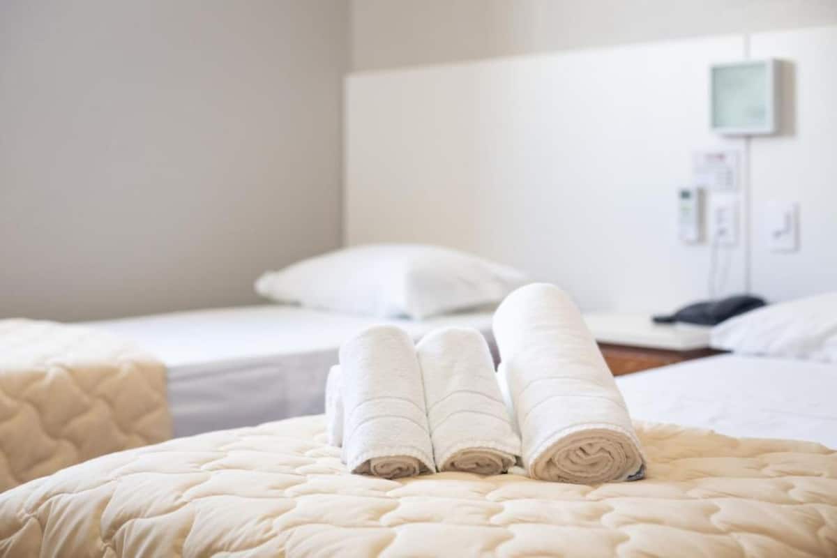 A hotel room with a neatly made bed, a bedside table, and a wall-mounted control panel.