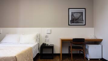 Ein Hotelzimmer mit Bett, Schreibtisch, Stuhl, kleinem Kühlschrank und einem gerahmten Bild an der Wand.