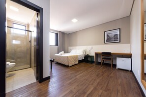 Ein Hotelzimmer mit Bett, Schreibtisch, Stuhl, Heizkörper und einer Duschkabine aus Glas.