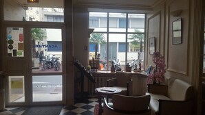 A hotel lobby with a checkered floor, a reception desk, and a view of the street outside. - ACANTHE HOTEL (Bordeaux)
