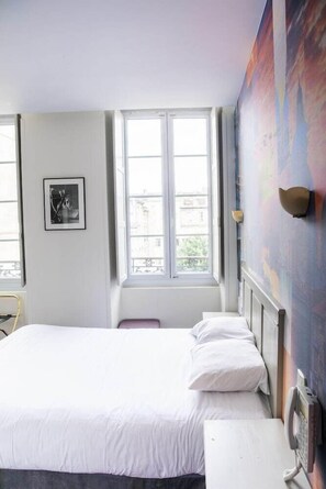 A hotel room with a bed, a window, a wall-mounted telephone, and a framed picture. - ACANTHE HOTEL (Bordeaux)