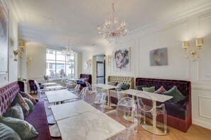 A spacious room with a large chandelier, clear dining tables, a plush sofa, and artwork on the walls. - ACANTHE HOTEL (Bordeaux)
