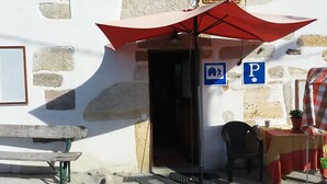 A stone building with a red umbrella, a bench, and a table with a red and yellow tablecloth. - Albergue A Casiña di Marcello - Hostel (Palas de Rei)