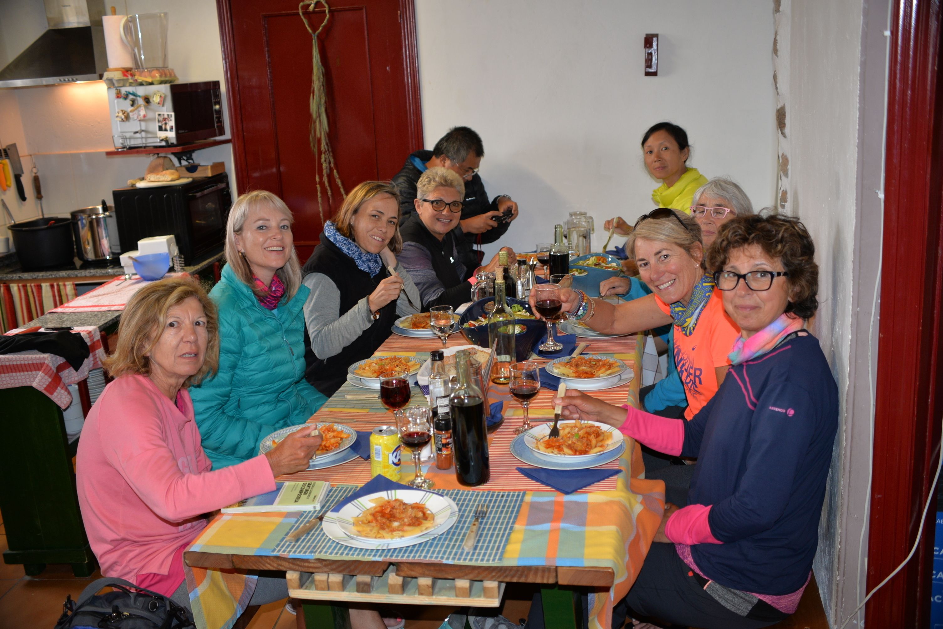 A group of people dining at a wooden table with plates of food, wine glasses, and a variety of condiments.