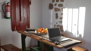 A wooden table with a laptop, a bowl of fruit, and a fire extinguisher on the wall. - Albergue A Casiña di Marcello - Hostel (Palas de Rei)