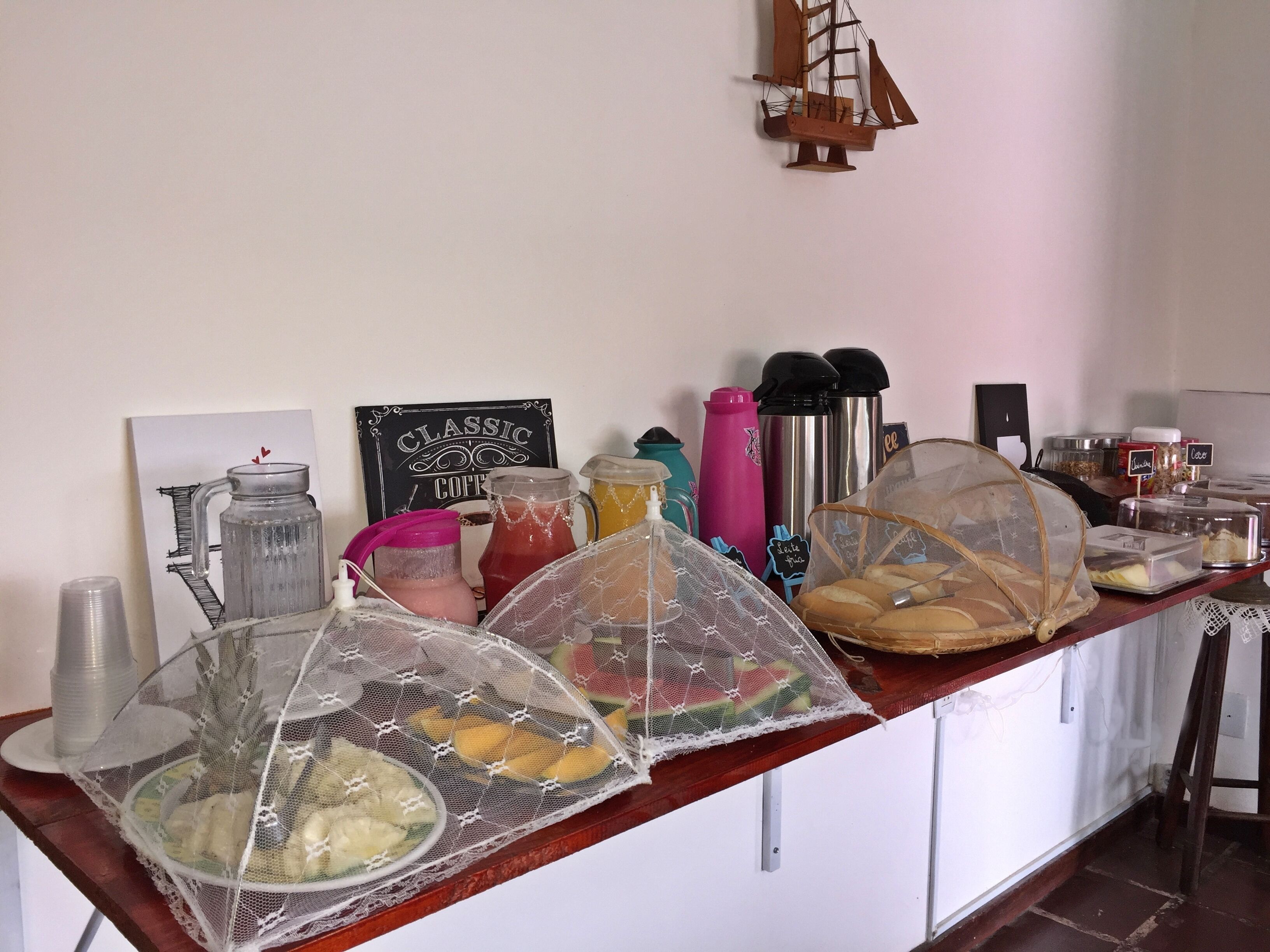 Uma mesa de pequeno-almoço com diversos alimentos, bebidas e um modelo decorativo de navio na parede.