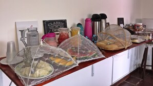 A breakfast bar with various food items, beverages, and a decorative ship model on the wall. - Pousada Azul dos Búzios (Búzios)