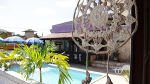 A pool area with a decorative rope hanging ornament, palm trees, and umbrellas. - Pousada Azul dos Búzios (Búzios)