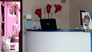 A reception desk with a laptop, a sign reading "RECEPC", and a wall with red flower paintings. - Pousada Azul dos Búzios (Búzios)