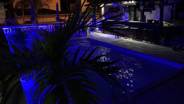 A nighttime outdoor pool area with blue lighting, a bar, and a restaurant named 'Heineken'. - Pousada Azul dos Búzios (Búzios)