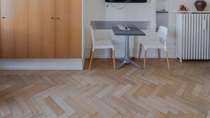 Una habitación con un armario de madera, una mesa de comedor con sillas, un televisor de pantalla plana montado en la pared y un radiador.