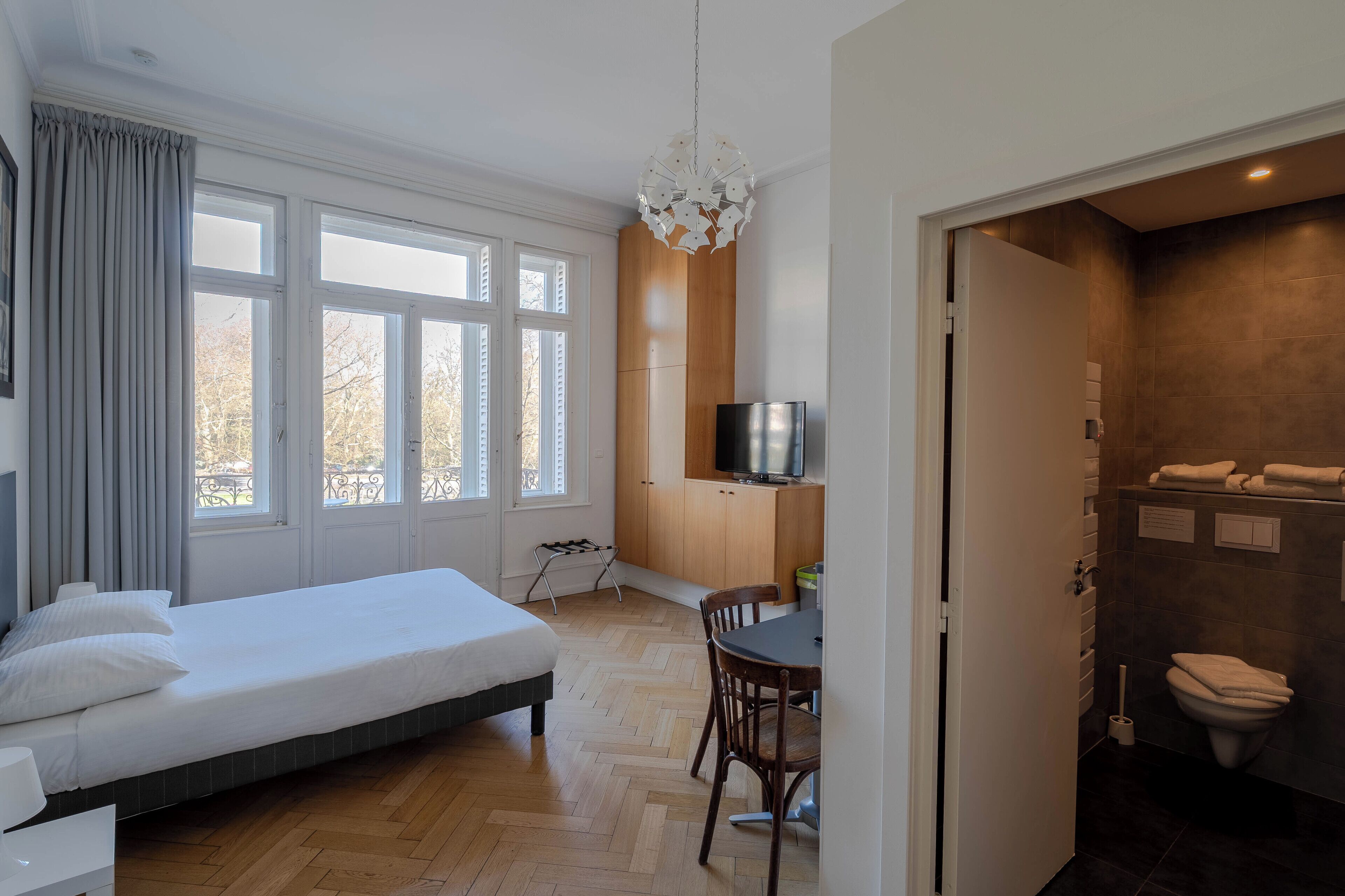 A hotel room with a bed, a desk, a chair, a TV, and a bathroom.