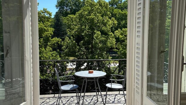 Puerta de vidrio que da a un patio exterior con una mesa y sillas, rodeado por una cerca de metal y árboles.