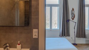 Un baño moderno con un espejo grande, lavamanos blanco y una botella de desinfectante de manos.