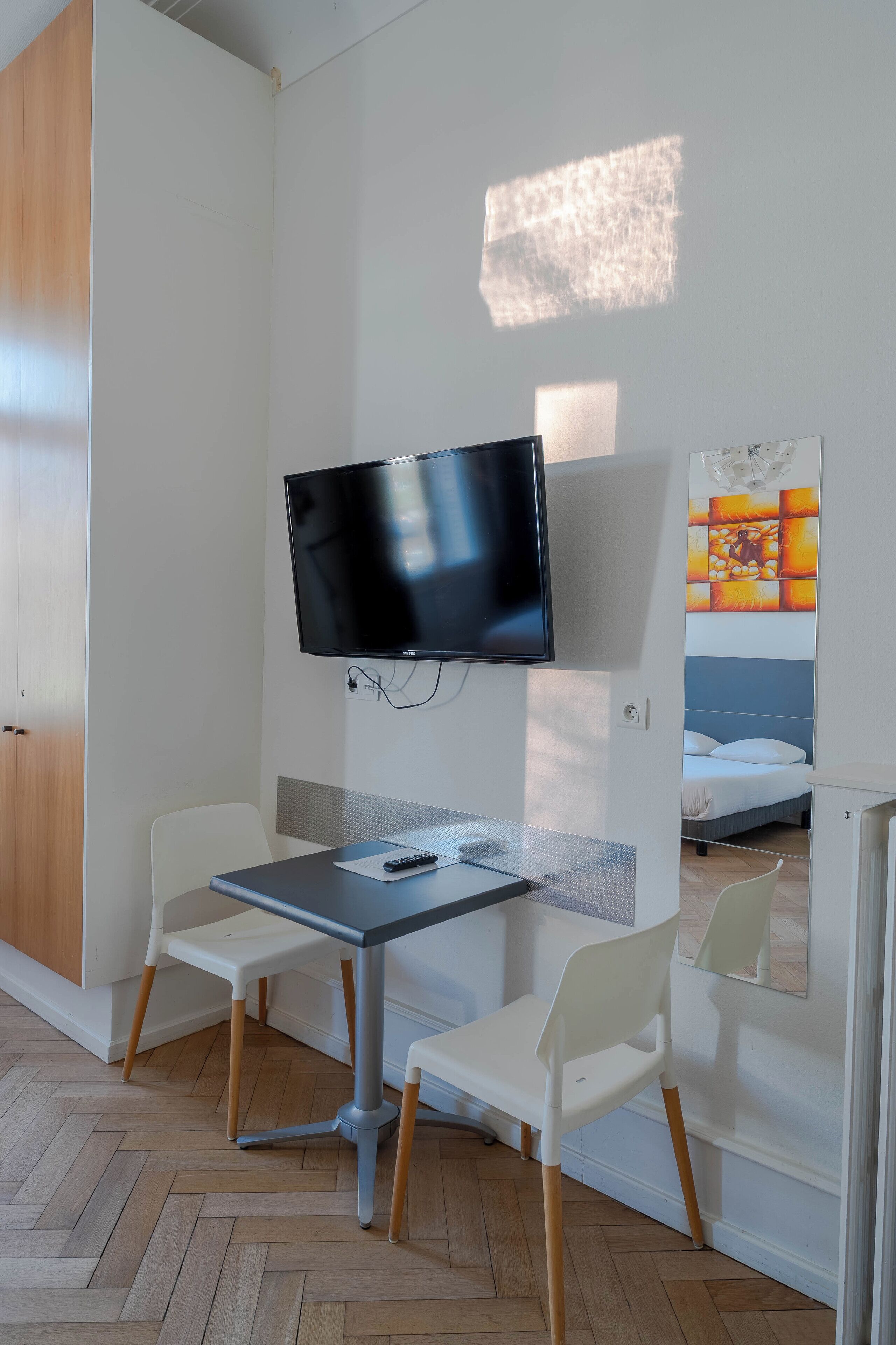 Een hotelkamer met een flatscreen televisie aan de muur, een klein tafeltje met een stoel en een bed met hoofdeinde.