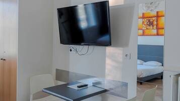 Een hotelkamer met een flatscreen televisie aan de muur, een klein tafeltje met een stoel en een bed met hoofdeinde.