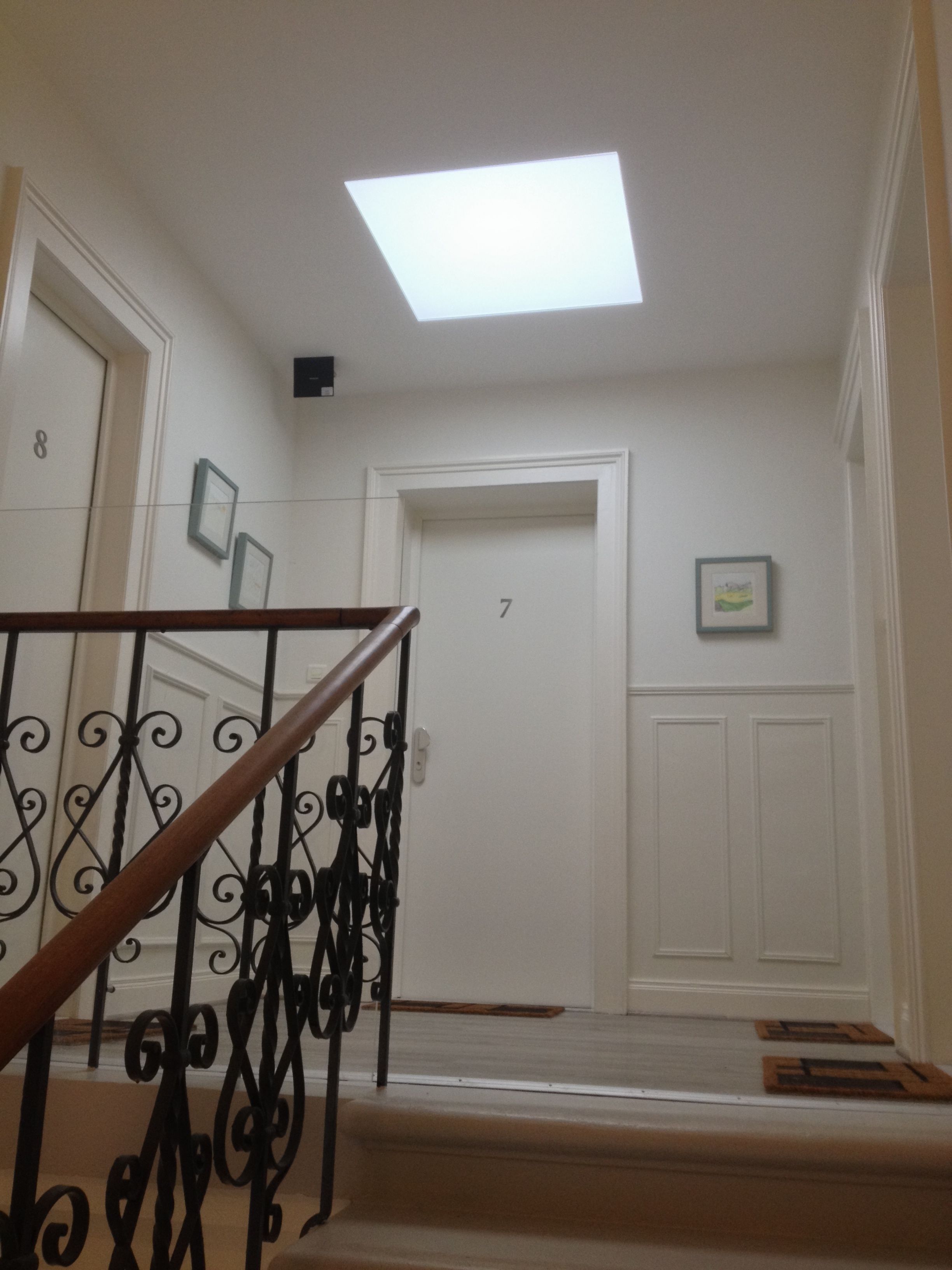 Un escalier doté d’une main courante en bois et de balustrades en métal noir, menant à une porte portant le numéro 7.