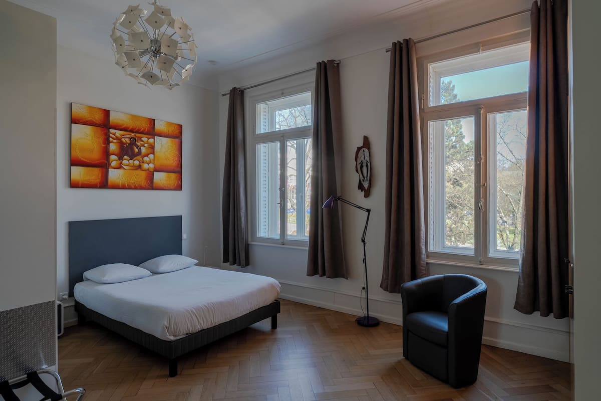 A bedroom with a bed, a chair, a desk, a lamp, and a window with curtains.